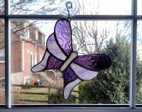 Stained glass butterfly suncatcher made with alternating purple cathedral glass and purple swirled opalescent glass with curled wire antennae.  Measures five and half inches in diameter and comes with a suction cup hanger.