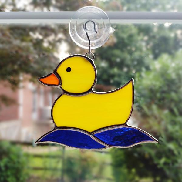 Yellow opalescent stained glass rubber duckie suncatcher with blue cathedral glass water waves underneath. Measures 5 1/4 inches by 4 inches, suction cup holder included. $35 plus $8.95 shipping