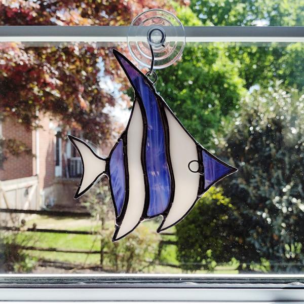 Stained glass angel fish suncatcher made with alternating purple and white wispy glass and white iridescent glass. Suction cup hanger included. Measures five inches by 6 inches.