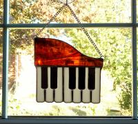 Stained glass piano suncatcher made with a brown swirled opalescent glass top with seven white glass keys and five black glass keys overlaid on top.  Measures six inches wide by five and half inches tall, with a hanging length of eight inches with the attached chain.  Comes with a suction cup hanger.