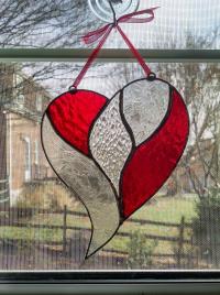 Stained glass unity heart suncatcher with a clear textured glass center surrounded by red cathedral glass and clear etch gluechip glass. Measures five inches by six inches and comes with a red ribbon and suction cup hanger.