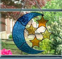Stained glass blue moon with four amber stars suncatcher made with textured cathedral glass, measuring seven inches by seven inches and comes with chain and suction cup hanger.