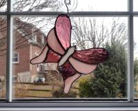 Pink stained glass butterfly suncatcher, made with alternating pink cathedral glass and pink opalescent glass with a white glass body. It measures five and half inches in diameter and comes with a suction cup hanger.