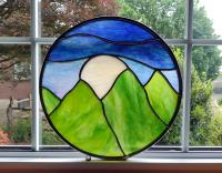 Ten inch round stained glass panel depicted green mountains, blue sky, with a large white moon rising between the mountain tops.