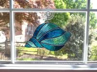 Stained glass conch shell suncatcher made with alternating turquoise and light aqua textured cathedral art glass. Measures seven inches wide by four and half inches tall and comes with a suction cup hanger. 