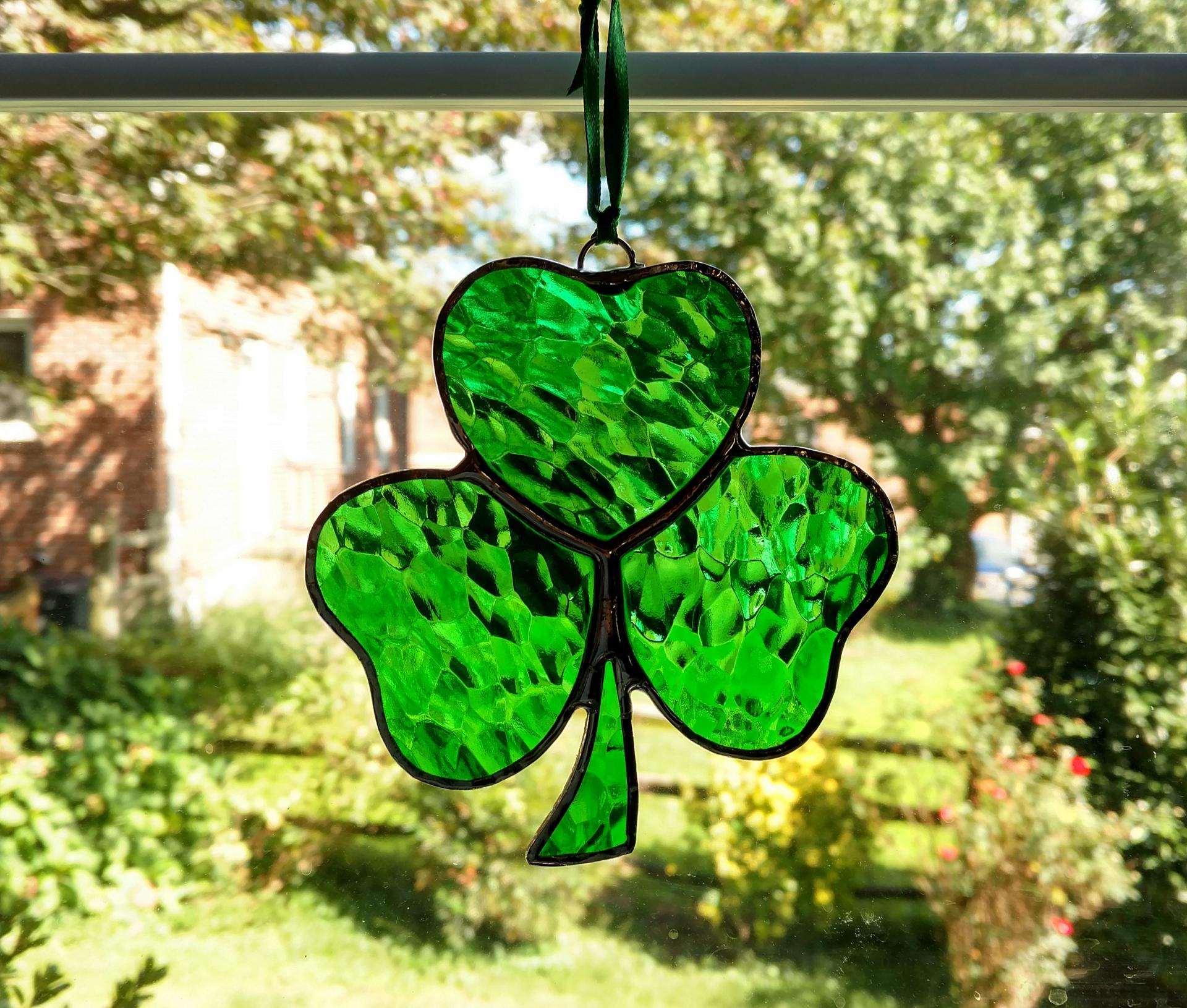 Stained glass shamrock suncatcher made with green hammered cathedral glass. Measures approximately four inches in diameter and comes with a suction cup hanger and ribbon.