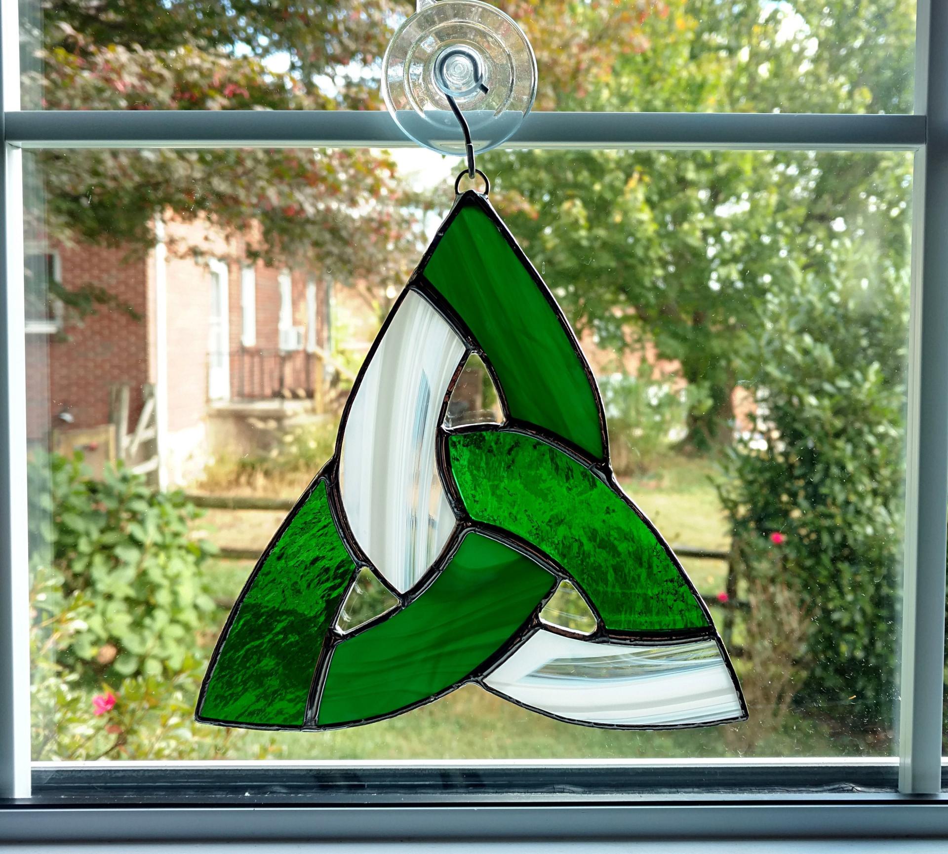 Seven inch diameter tricolor stained glass celtic knot suncatcher using green cathedral glass, green opalescent glass, and white and clear wispy glass. Suction cup hanger included.