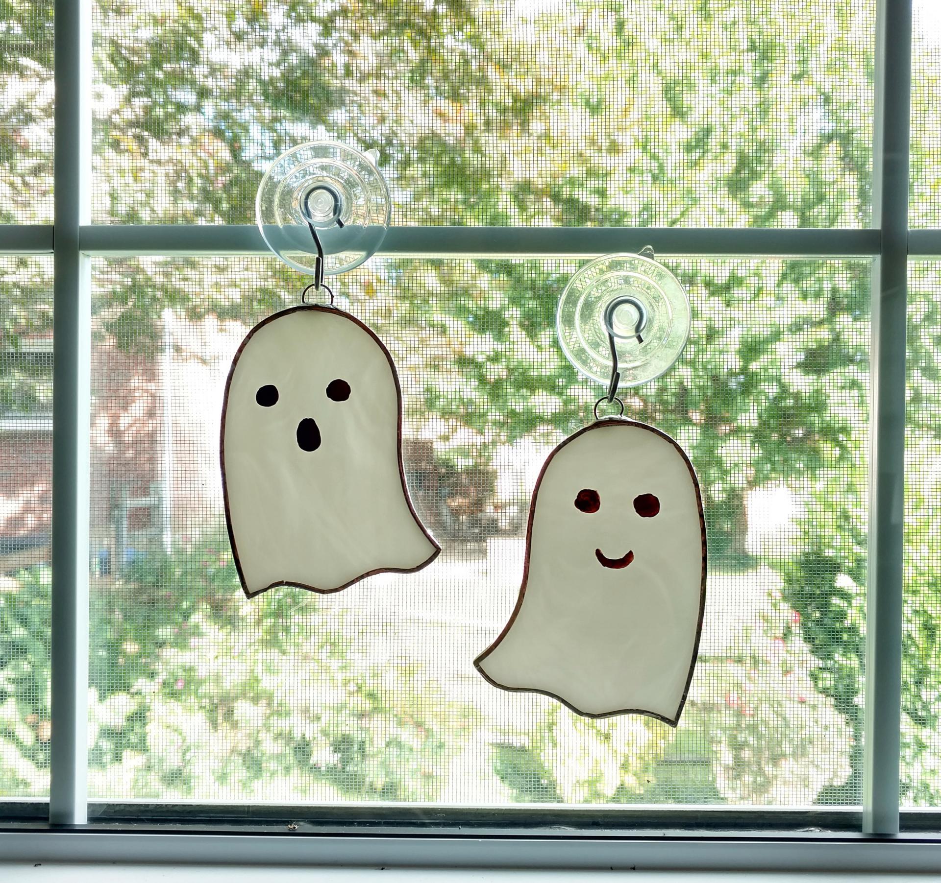 white opalescent stained glass ghost suncatchers with scary or happy faces painted on them. Measuring three inches by four inches and come with suction cup hangers. Your choice of face type. Priced at fifteen dollars each or thirty dollars for a set.