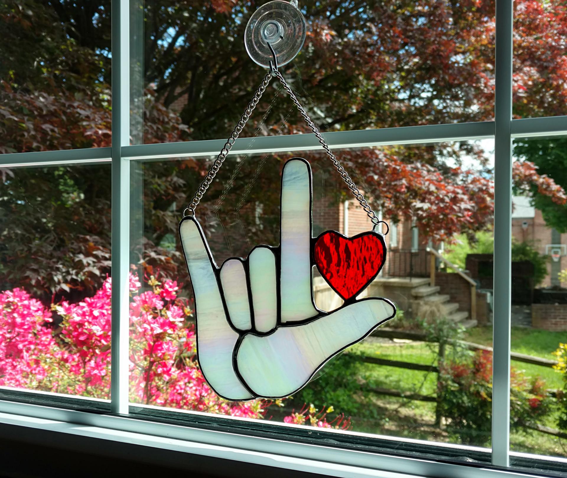 Stained Glass I Love you American sign language suncatcher with red heart, made with white iridescent art glass for the hand and red cathedral glass for the heart. Measure six inches by six and half inches, suction cup holder included.