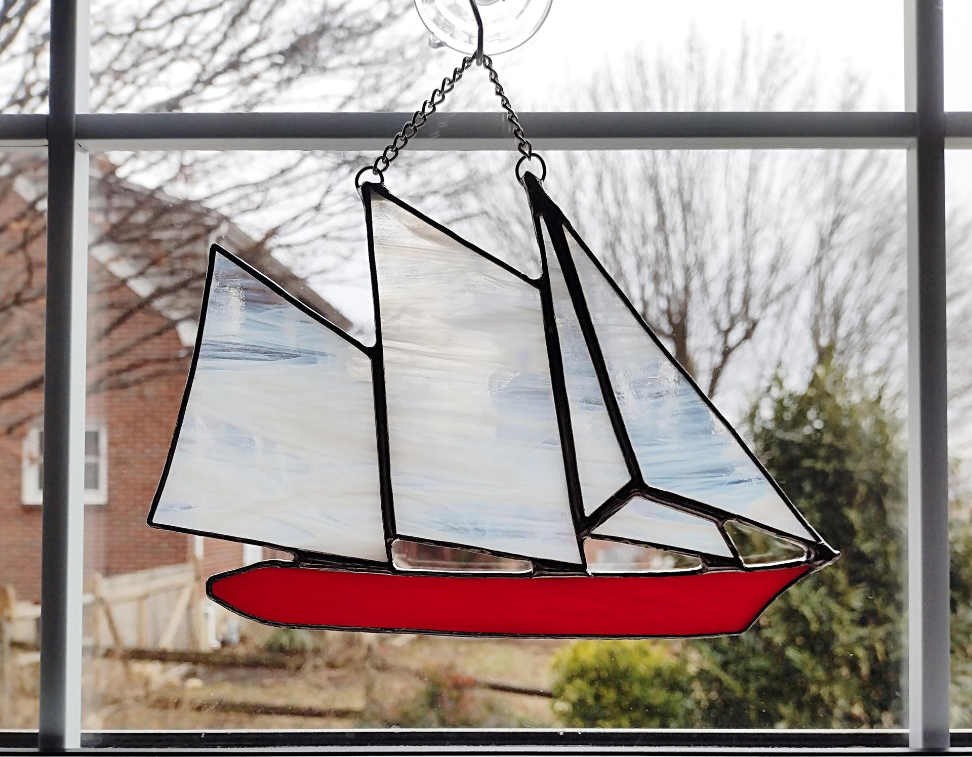 stained glass sailboat schooner suncatcher with a red hull and white and clear swirled sails. 6 in by 8 in plus chain.