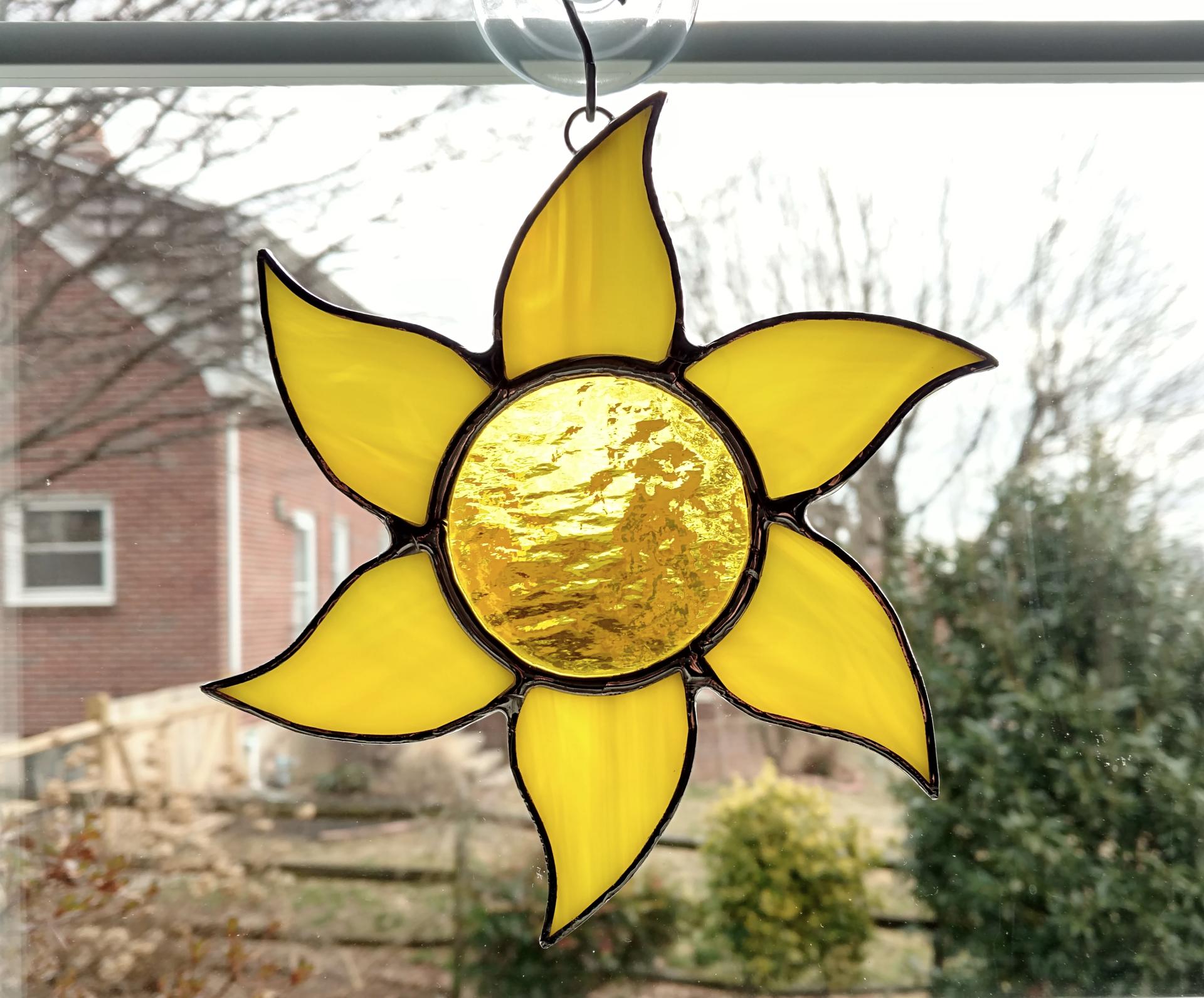 Stained glass sun suncatcher made with a yellow textured cathedral glass center surrounded by yellow swirled opalescent glass rays.  Measures 6 inches in diameter and comes with a suction cup hanger.