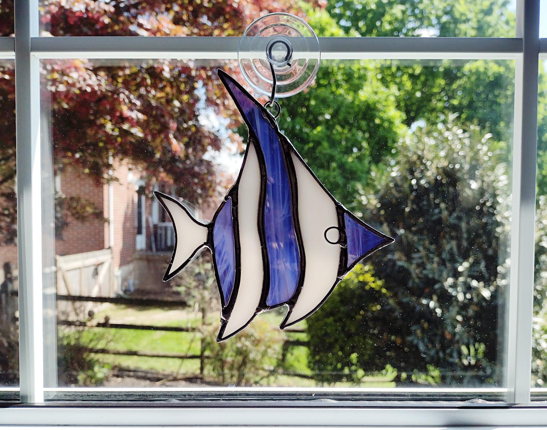 Stained glass angel fish suncatcher made with alternating purple and white wispy glass and white iridescent glass. Suction cup hanger included. Measures five inches by 6 inches.