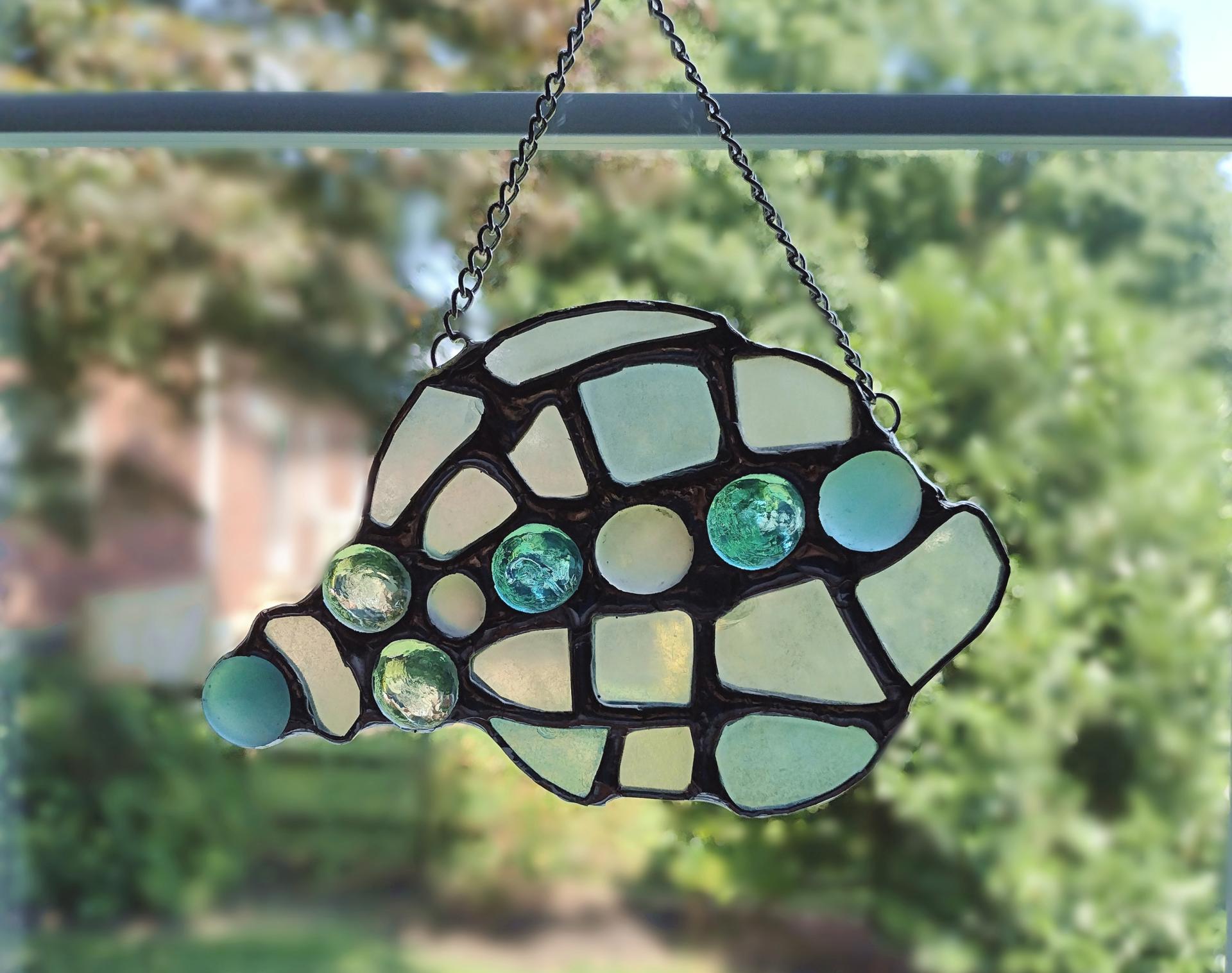 conch shell suncatcher made with pale blue, green, and yellow sea glass and glass jewels, measures approximately seven inches by four inches, attached chain and suction cup holder included.