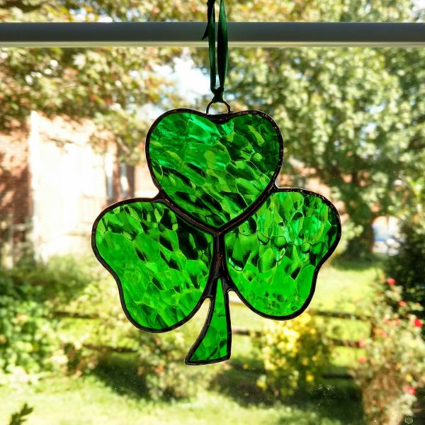 Stained glass shamrock suncatcher made with green hammered cathedral glass. Measures approximately four inches in diameter and comes with a suction cup hanger and ribbon.