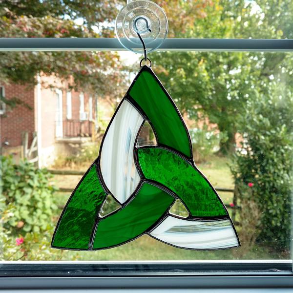 Seven inch diameter tricolor stained glass celtic knot suncatcher using green cathedral glass, green opalescent glass, and white and clear wispy glass. Suction cup hanger included.