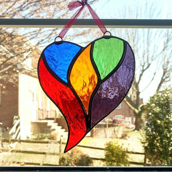 rainbow stained glass heart suncatcher measuring five inches by six inches.  Made with blue, green, amber, purple, and red cathedral glass and comes with a suction cup hanger and red ribbon.