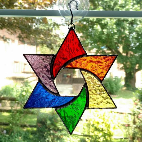 Stained glass star of David made with rainbow colors of red, orange, yellow, green, purple, and blue textured cathedral art glass.  Measures six inches in diameter and comes with a suction cup hanger.