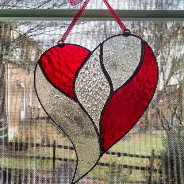 Stained glass unity heart suncatcher with a clear textured glass center surrounded by red cathedral glass and clear etch gluechip glass. Measures five inches by six inches and comes with a red ribbon and suction cup hanger.