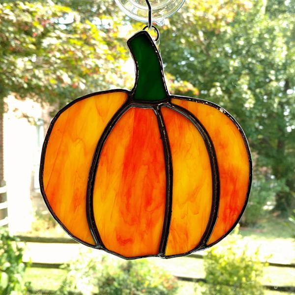 Stained glass pumpkin suncatcher made with orange and green opalescent art glass and measuring five inches in diameter. Comes with a suction cup hanger.