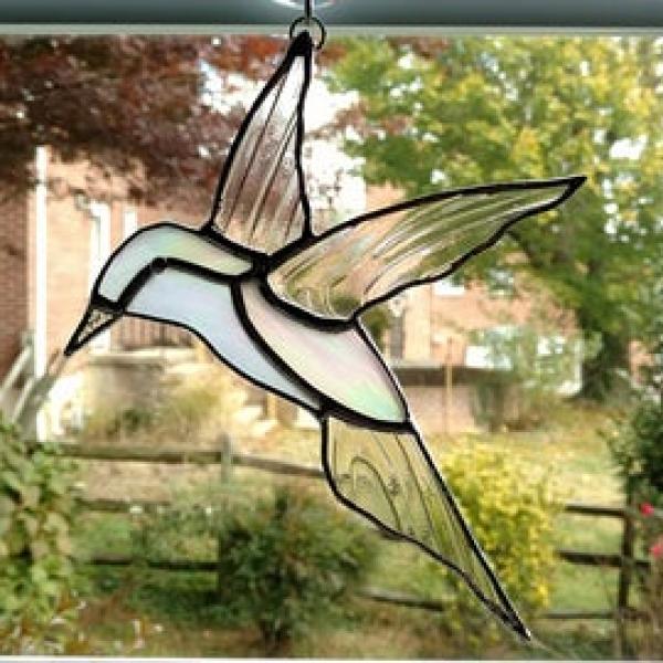 Stained glass hummingbird suncatcher made with white iridescent glass and clear swirled glass wings. Measures eight inches long by six and half inches wide and comes with a suction cup hanger.