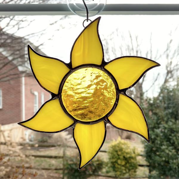 Stained glass sun suncatcher made with a yellow textured cathedral glass center surrounded by yellow swirled opalescent glass rays.  Measures 6 inches in diameter and comes with a suction cup hanger.