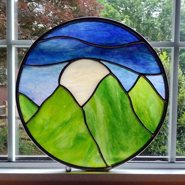 Ten inch round stained glass panel depicted green mountains, blue sky, with a large white moon rising between the mountain tops.