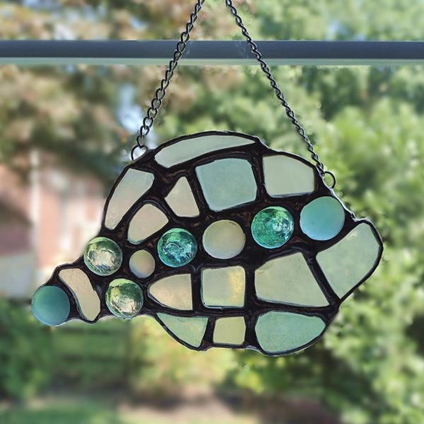 conch shell suncatcher made with pale blue, green, and yellow sea glass and glass jewels, measures approximately seven inches by four inches, attached chain and suction cup holder included.