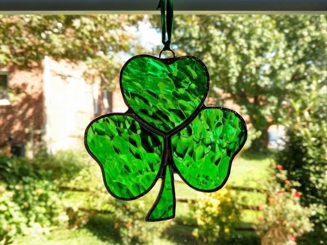 Stained glass shamrock suncatcher made with green hammered cathedral glass. Measures approximately four inches in diameter and comes with a suction cup hanger and ribbon.