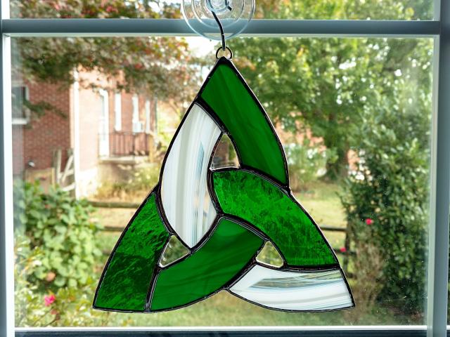 Seven inch diameter tricolor stained glass celtic knot suncatcher using green cathedral glass, green opalescent glass, and white and clear wispy glass. Suction cup hanger included.