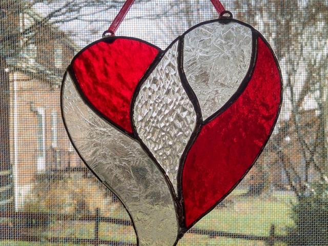 Stained glass unity heart suncatcher with a clear textured glass center surrounded by red cathedral glass and clear etch gluechip glass. Measures five inches by six inches and comes with a red ribbon and suction cup hanger.
