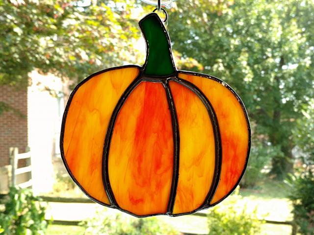 Stained glass pumpkin suncatcher made with orange and green opalescent art glass and measuring five inches in diameter. Comes with a suction cup hanger.