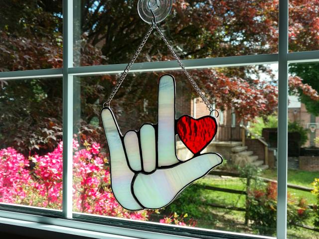 Stained Glass I Love you American sign language suncatcher with red heart, made with white iridescent art glass for the hand and red cathedral glass for the heart. Measure six inches by six and half inches, suction cup holder included.