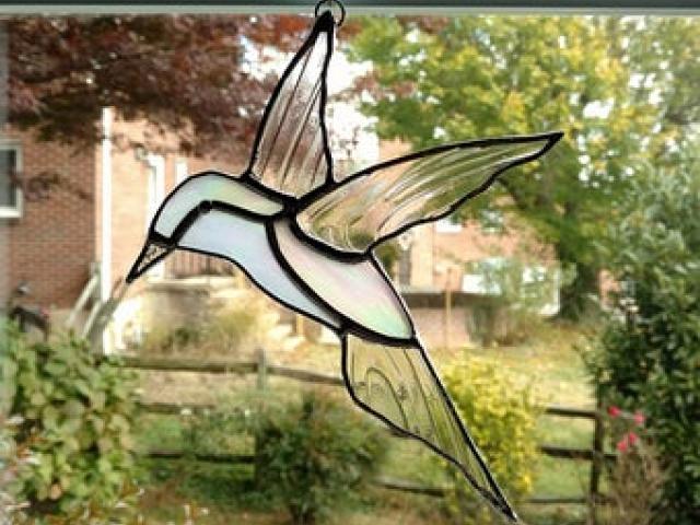 Stained glass hummingbird suncatcher made with white iridescent glass and clear swirled glass wings. Measures eight inches long by six and half inches wide and comes with a suction cup hanger.