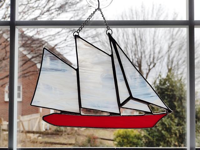 stained glass sailboat schooner suncatcher with a red hull and white and clear swirled sails. 6 in by 8 in plus chain.