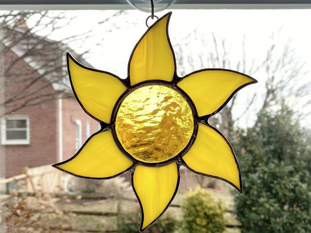 Stained glass sun suncatcher made with a yellow textured cathedral glass center surrounded by yellow swirled opalescent glass rays.  Measures 6 inches in diameter and comes with a suction cup hanger.