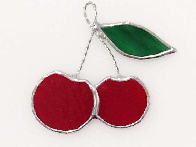 stained glass cherry cluster suncatcher with two red glass cherries and one green glass leave on twisted wire stems.  Measures three and half inches by four inches and comes with a suction cup hanger.