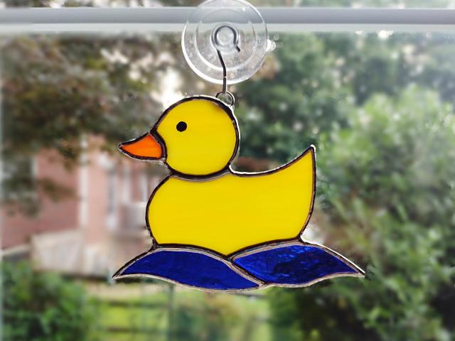 Yellow opalescent stained glass rubber duckie suncatcher with blue cathedral glass water waves underneath. Measures 5 1/4 inches by 4 inches, suction cup holder included. $35 plus $8.95 shipping