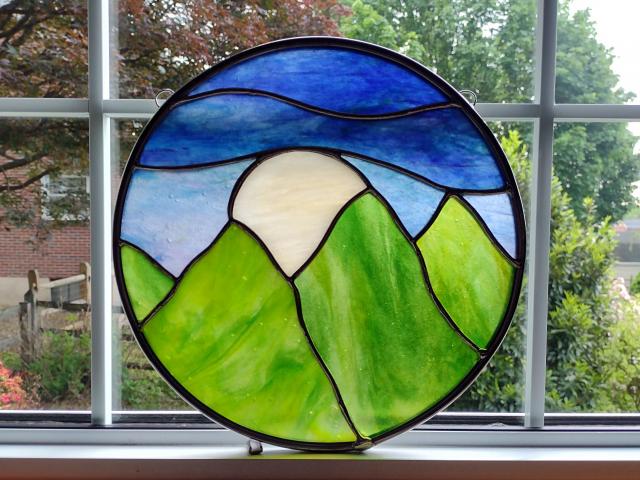 Ten inch round stained glass panel depicted green mountains, blue sky, with a large white moon rising between the mountain tops.